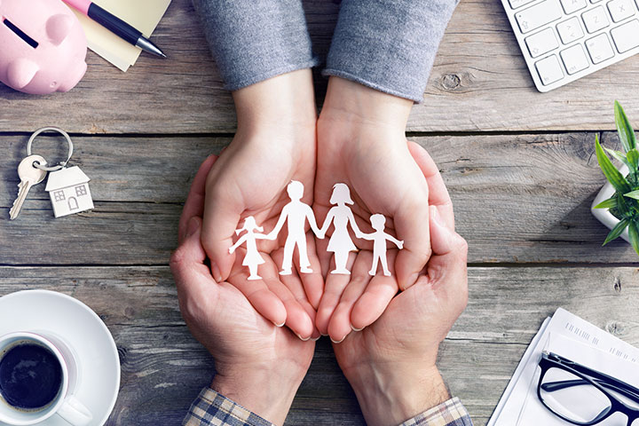 People's hands holding a paper cutout of a family.